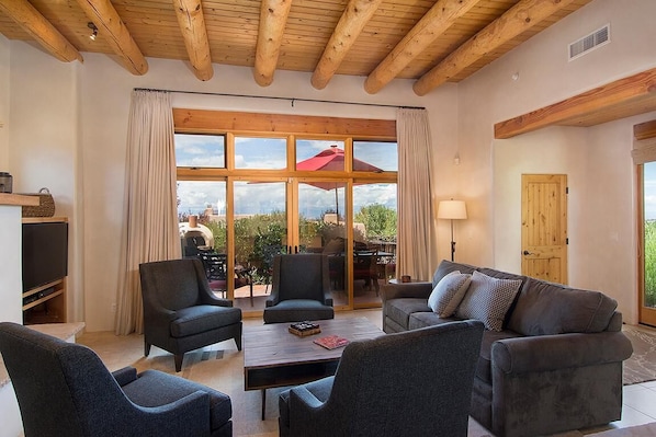 A spacious living room with a large window, wooden ceiling beams, and a cozy seating area.