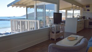 A spacious balcony with a view of the ocean and pier, a small kitchen area, and a seating area with a television. - Breathtaking Ocean and Beach Views (Avila Beach)