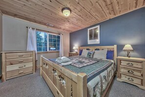 A bedroom with a wooden bed, two bedside tables, a window with curtains, and a ceiling light.