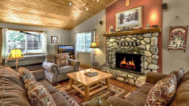 A cozy living room with a stone fireplace, wooden ceiling, and comfortable seating.