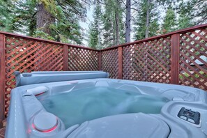 A hot tub surrounded by a wooden lattice fence with tall trees in the background.