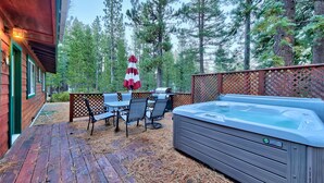 A wooden deck with a hot tub, outdoor seating, and a view of a forest.