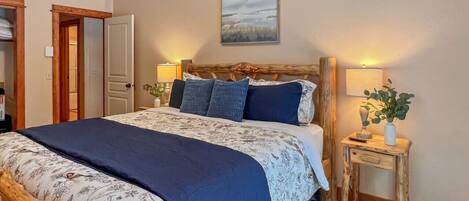A bedroom with a bed, bedside tables, a nightstand, a door, and a wall-mounted painting.