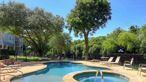 Una piscina con sillas de descanso, un jacuzzi y un área cercada con árboles.