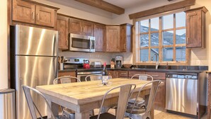 Eine moderne Küche mit Holzschränken, Edelstahlgeräten, einem Esstisch mit Stühlen und einem Fenster mit Blick auf die Berge.