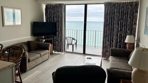 Un salon comprenant un canapé, un fauteuil, un téléviseur et offrant une vue sur l’océan grâce à de grandes fenêtres.