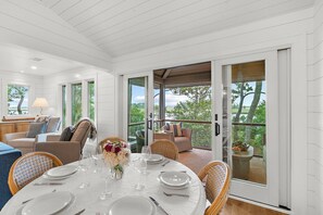 A dining area with a round table set for four, surrounded by wicker chairs, a vase of flowers, and a view of the outdoors through large sliding glass doors.