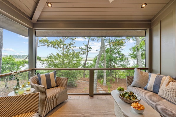A balcony with wicker furniture, a bowl of fruit, and a glass of drink.