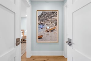 A hallway with a framed photograph on the wall, a wooden floor, and white doors.
