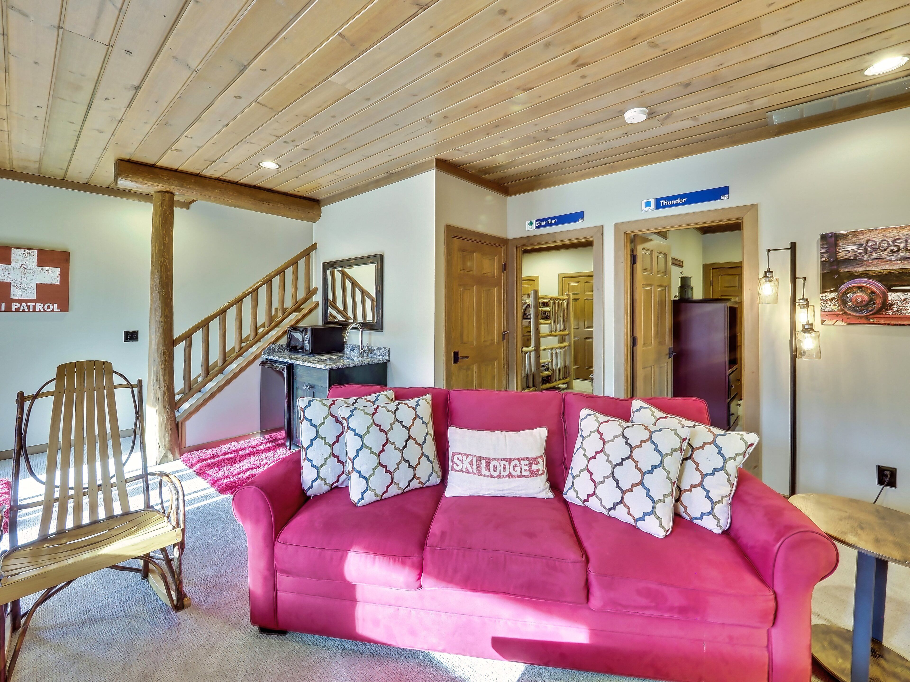 A cozy living room with a pink sofa, wooden chair, and a staircase.