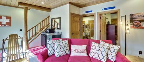 A cozy living room with a pink sofa, wooden chair, and a staircase.