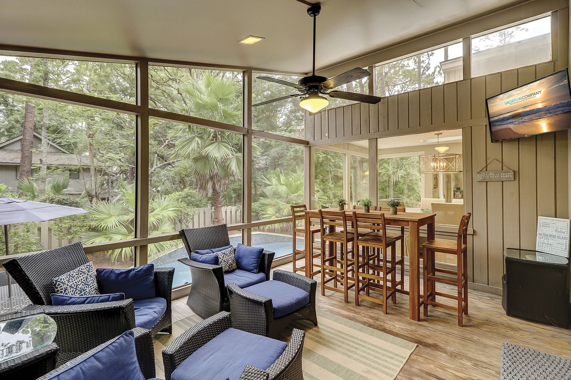 A spacious balcony with wicker furniture, a wooden dining table, and a TV mounted on the wall.