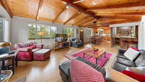 A spacious living area with a high wooden ceiling, large windows, a cozy seating arrangement, and a kitchen in the background. - Three Gazing Stars: Spacious, Stunning Views, Walk-to-Town, A/C (Idyllwild)