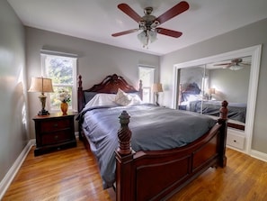 Quarto com cama de madeira, duas mesas de cabeceira, um ventilador de teto e um espelho grande.