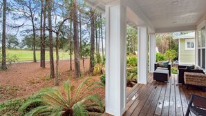 Een overdekt terras met uitzicht op een golfbaan en een huis.
