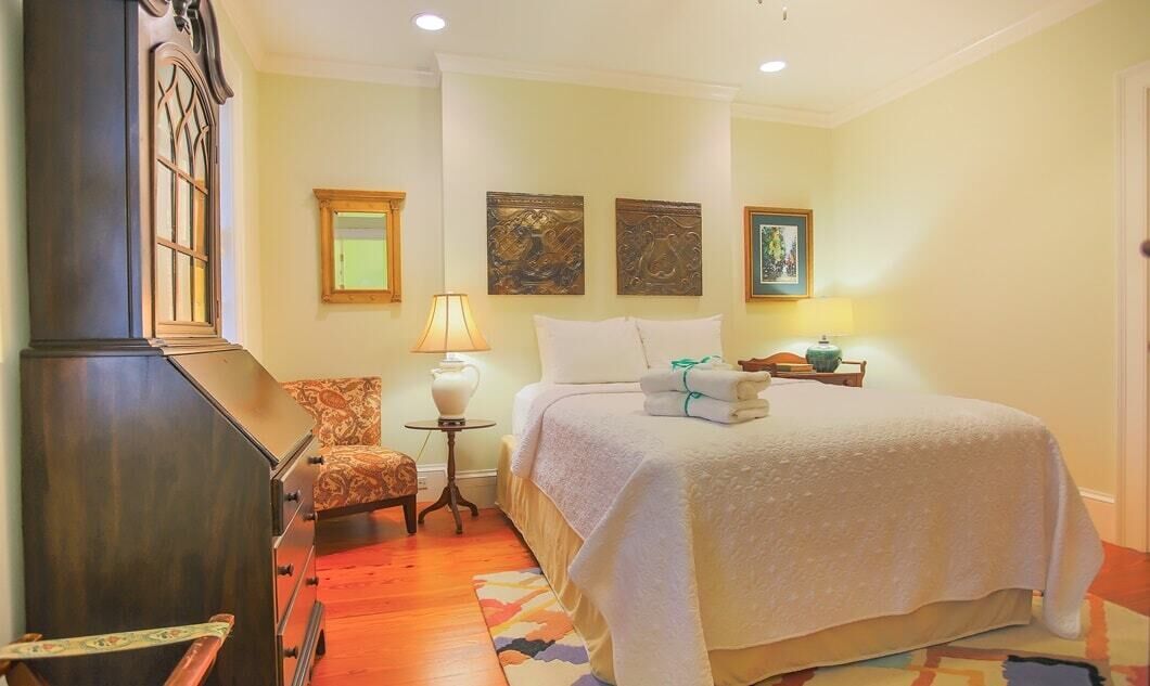 A bedroom with a bed, a chair, a nightstand, and a lamp.
