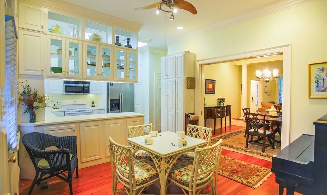 Una cocina amplia con muebles blancos, un comedor con sillas de mimbre y un piano en la esquina.