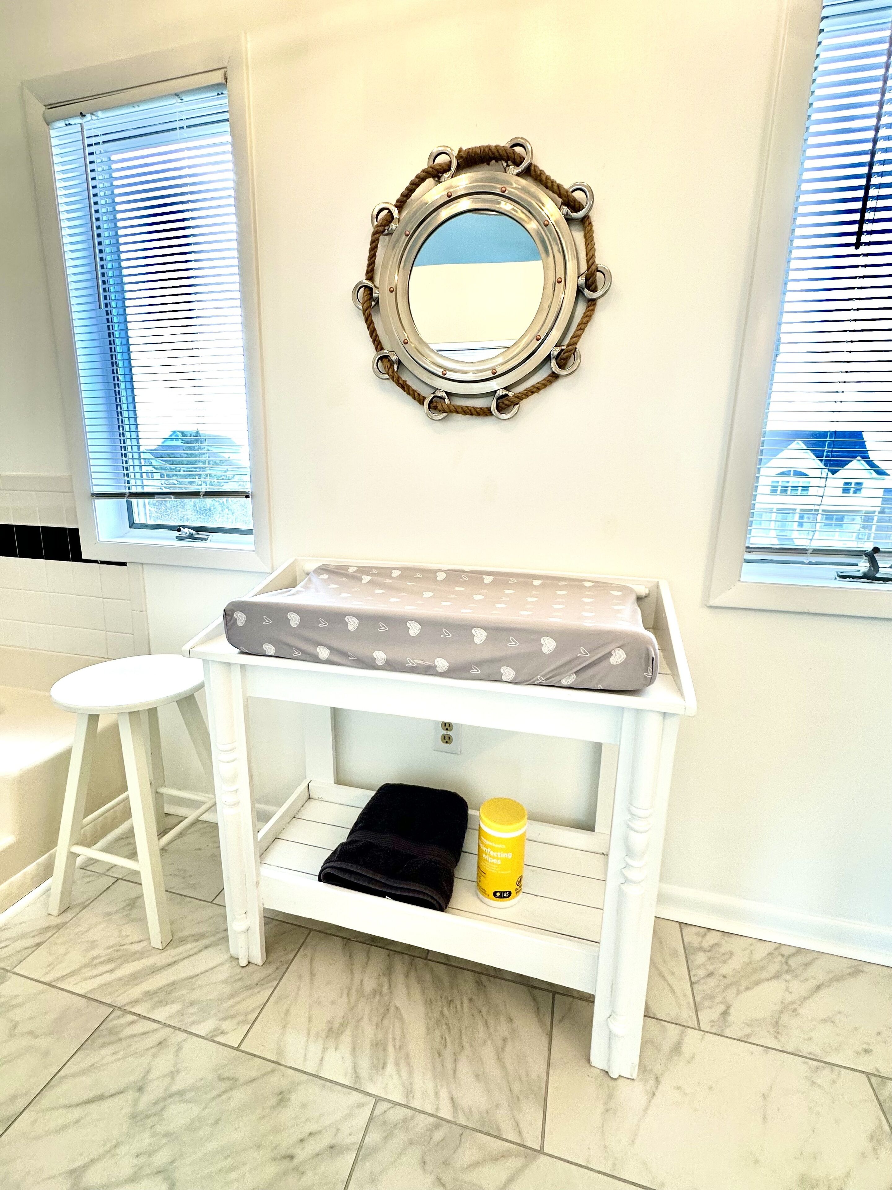 A bathroom with a white vanity, a mirror with a rope frame, and a window with blinds.
