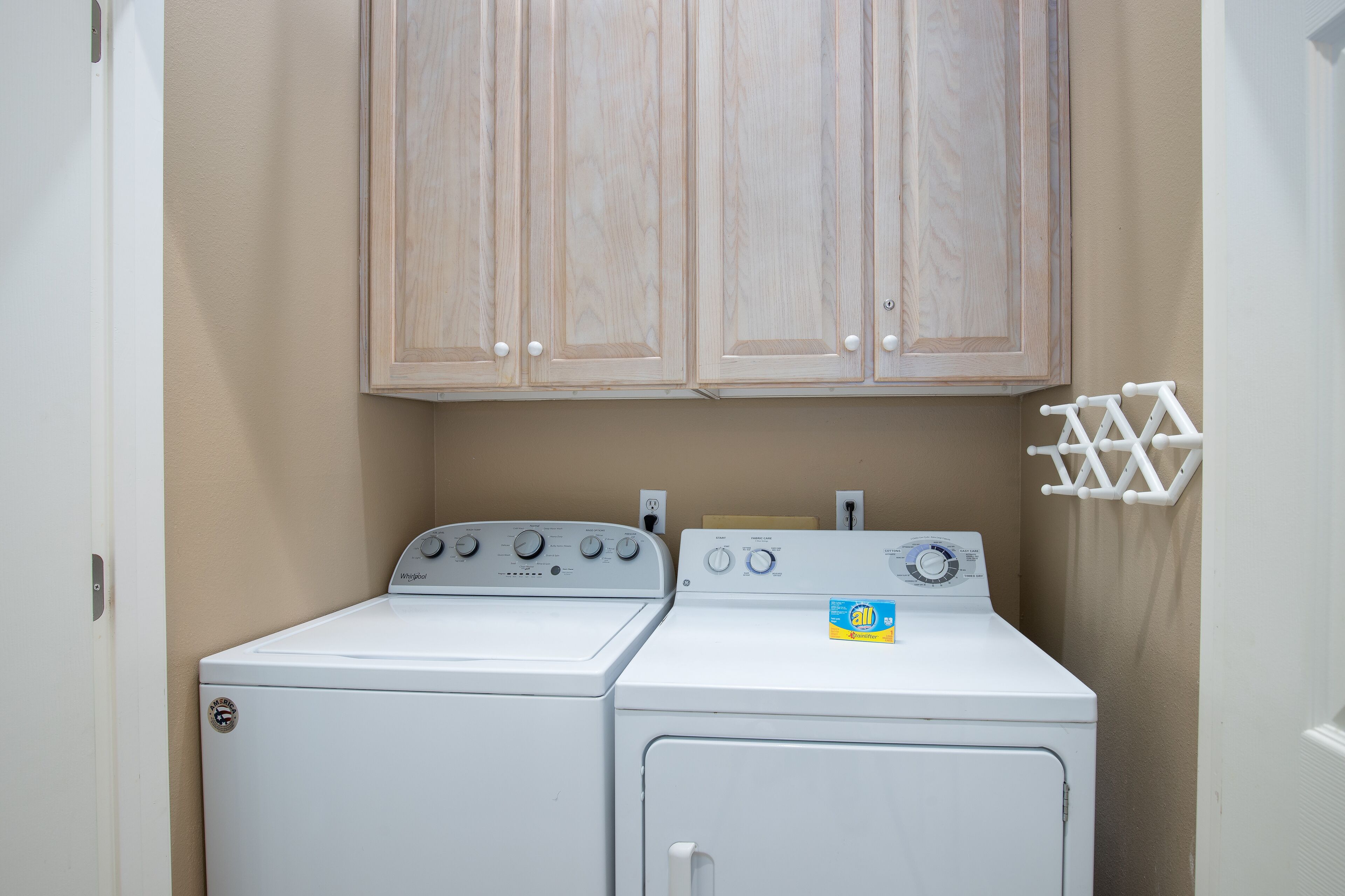 A laundry room with two white front-loading washers and dryers, beige walls, and wooden cabinets above.