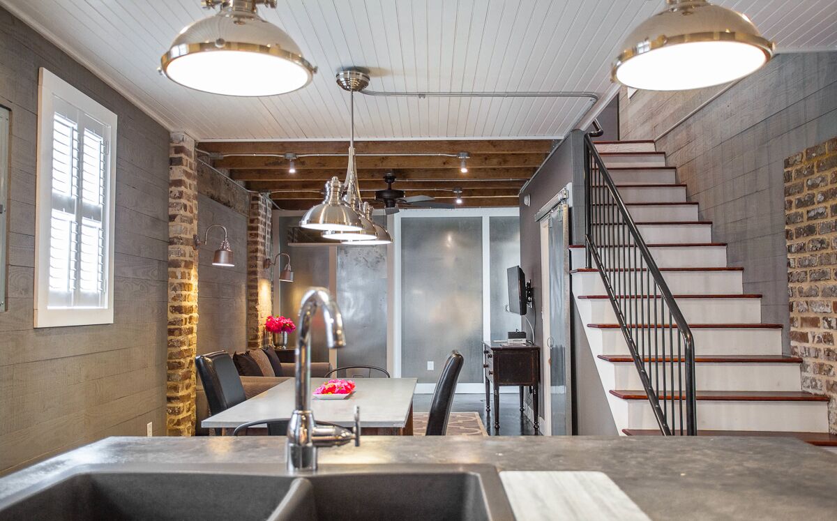 A modern kitchen with a large island, pendant lighting, and a staircase with a metal railing.