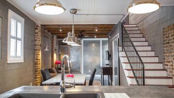 A modern kitchen with a large island, pendant lighting, and a staircase with a metal railing.