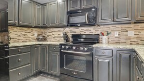 A kitchen with dark cabinets, a microwave, a stove, and a tiled backsplash. - 2BR Slopeside Disciples Village 691 - Amazing Ski In/Ski Out on Boyneland! (Boyne Falls)