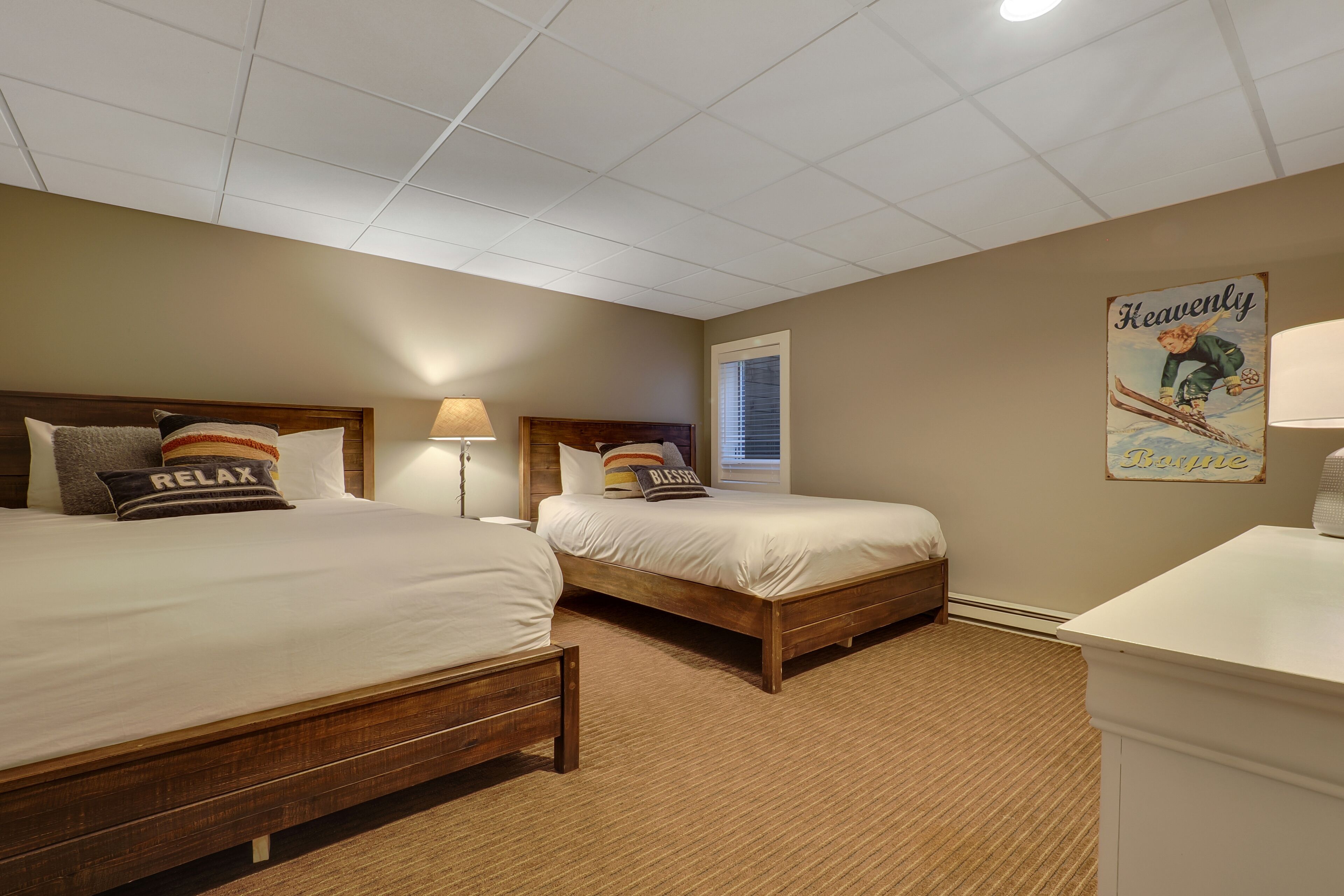 A bedroom with two beds, a wooden headboard, a lamp, and a poster on the wall.