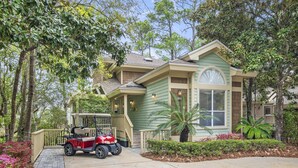 A two-story house with a green exterior, a covered porch, and a red golf cart parked in front. - Gated Resort ~ Golf Cart ~ Outdoor Deck (Miramar Beach)