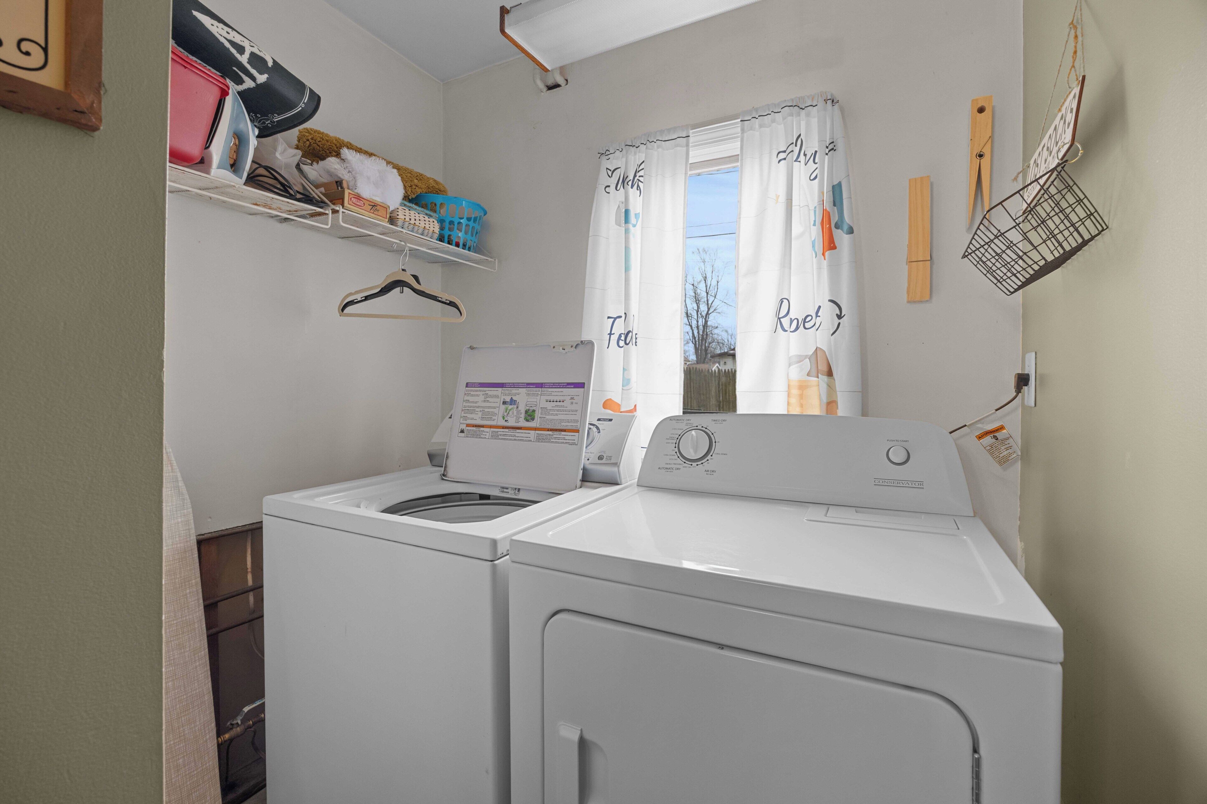A laundry area with two washing machines, a drying rack, and a window with a view.