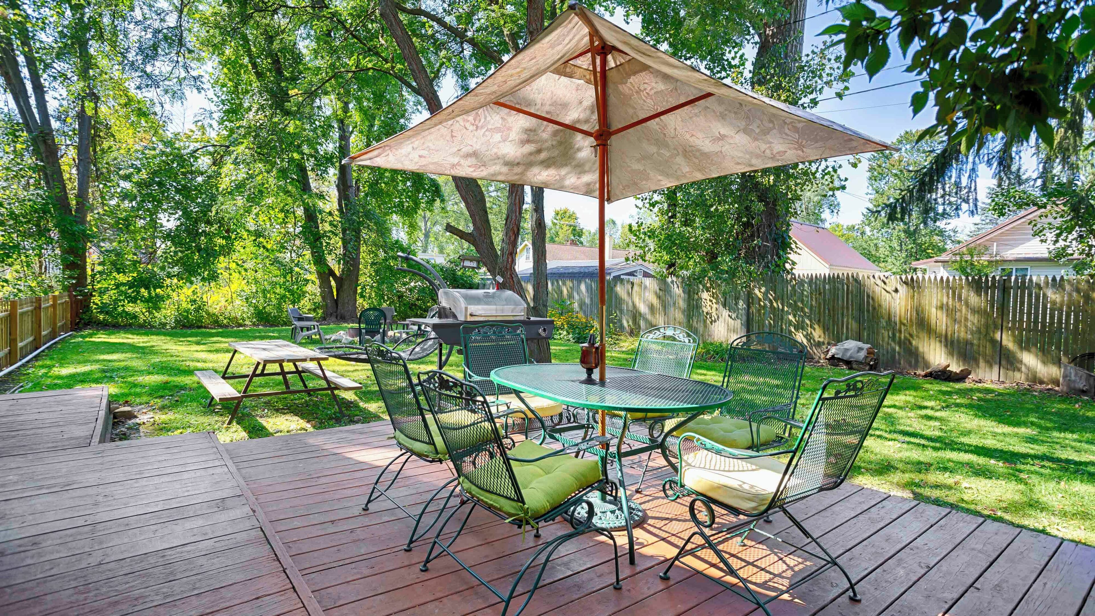 Une terrasse à l’arrière de la maison, avec une table et des chaises, un barbecue et une plateforme en bois.