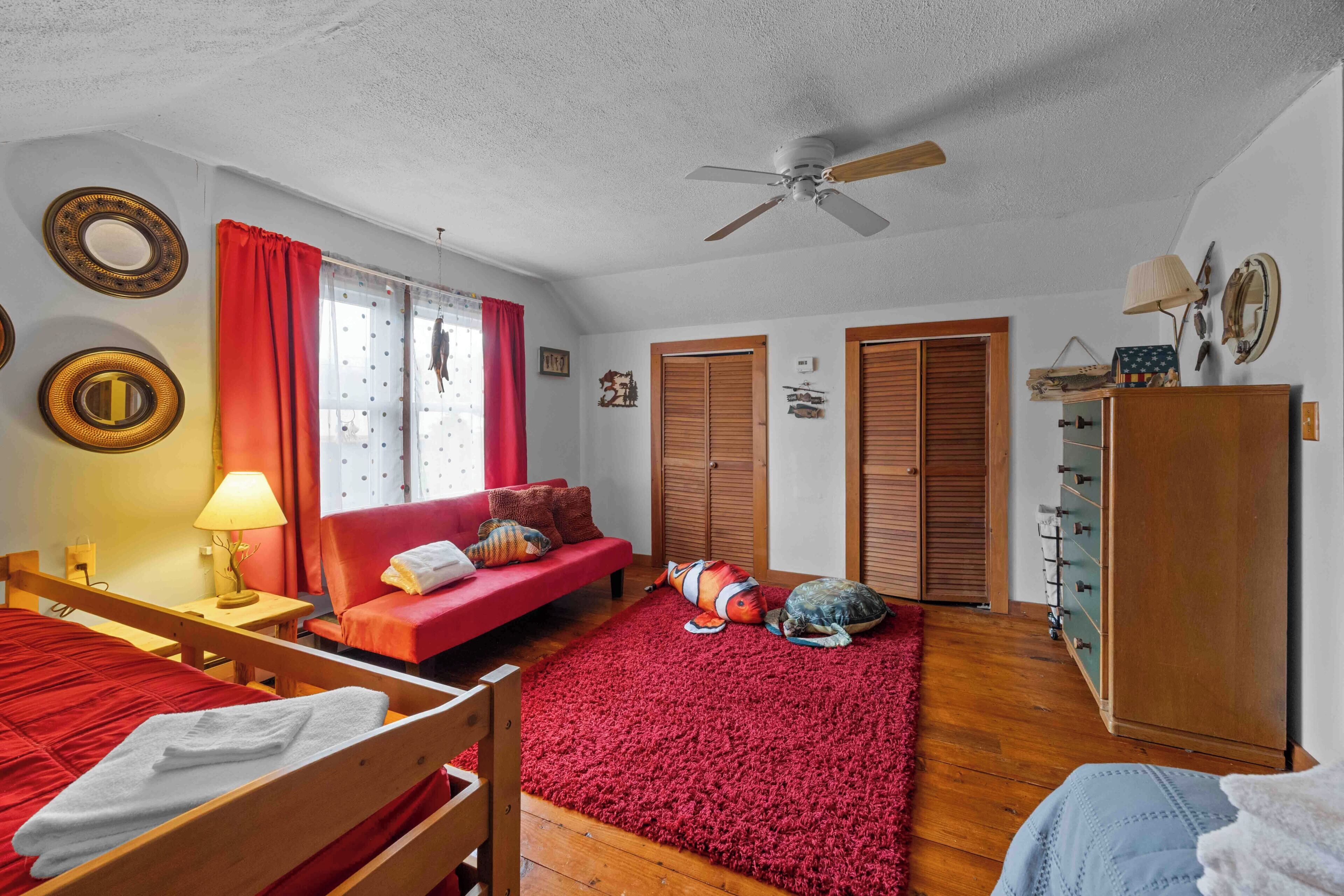 Een kamer met een bed, een rode bank, een houten garderobe, een plafondventilator en een rood vloerkleed.