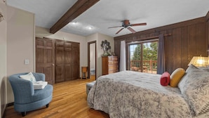 Une chambre à coucher avec un lit, une chaise, un plancher en bois, un ventilateur de plafond et une vue par la fenêtre.