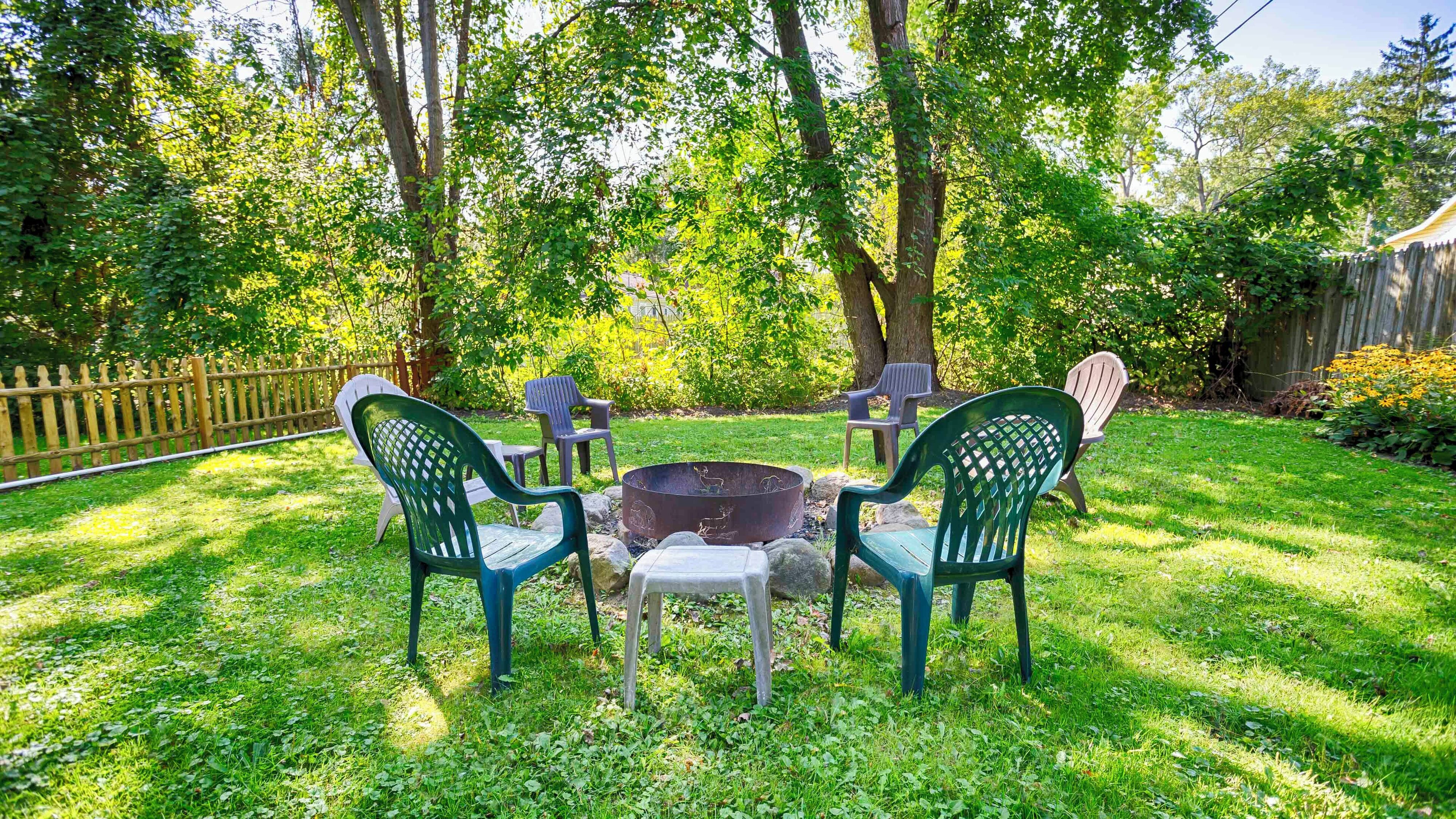A backyard with a fire pit, green chairs, and a wooden fence.