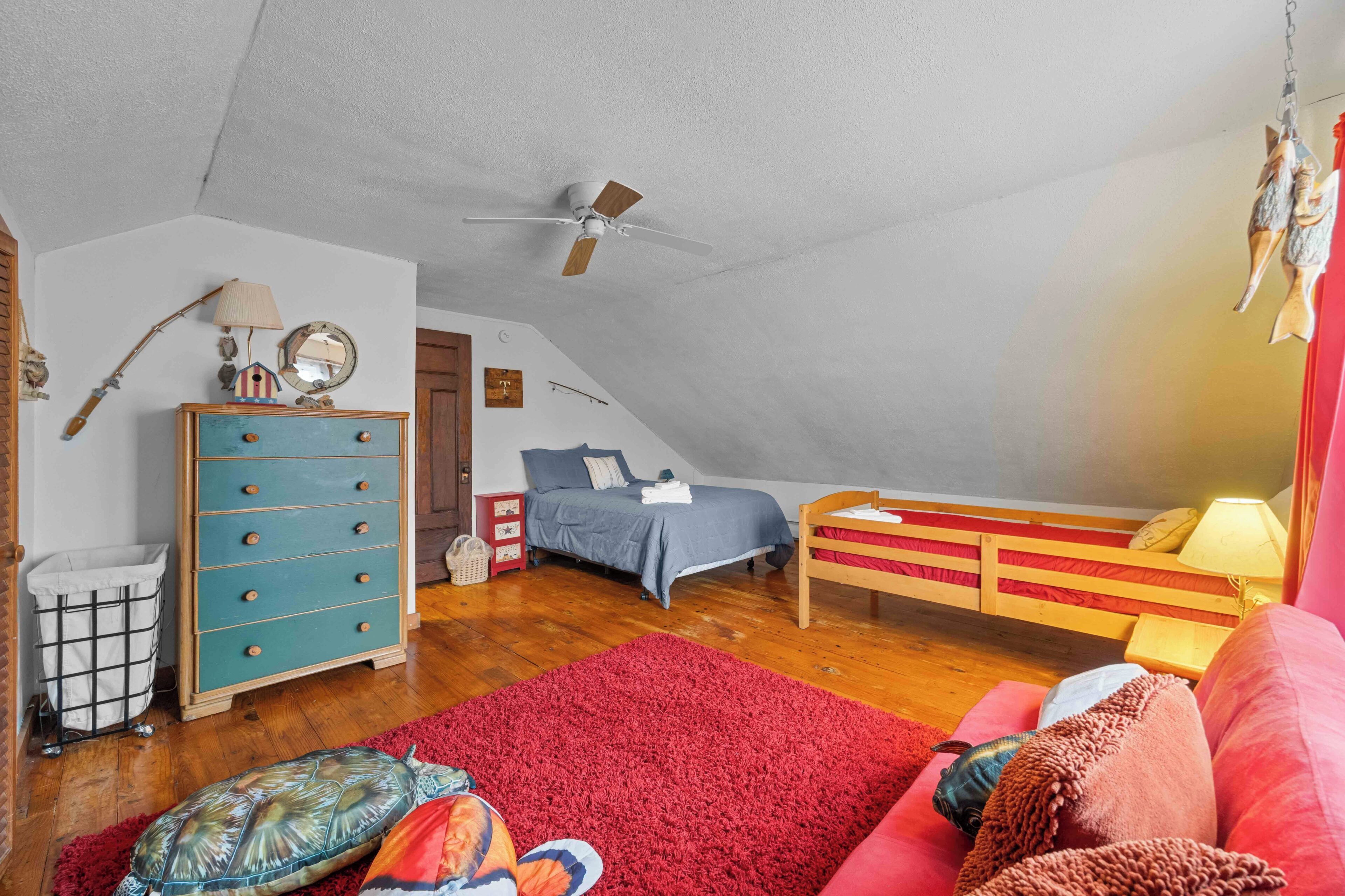 Quarto com cama, cômoda, ventilador de teto, tapete vermelho e sofá vermelho.