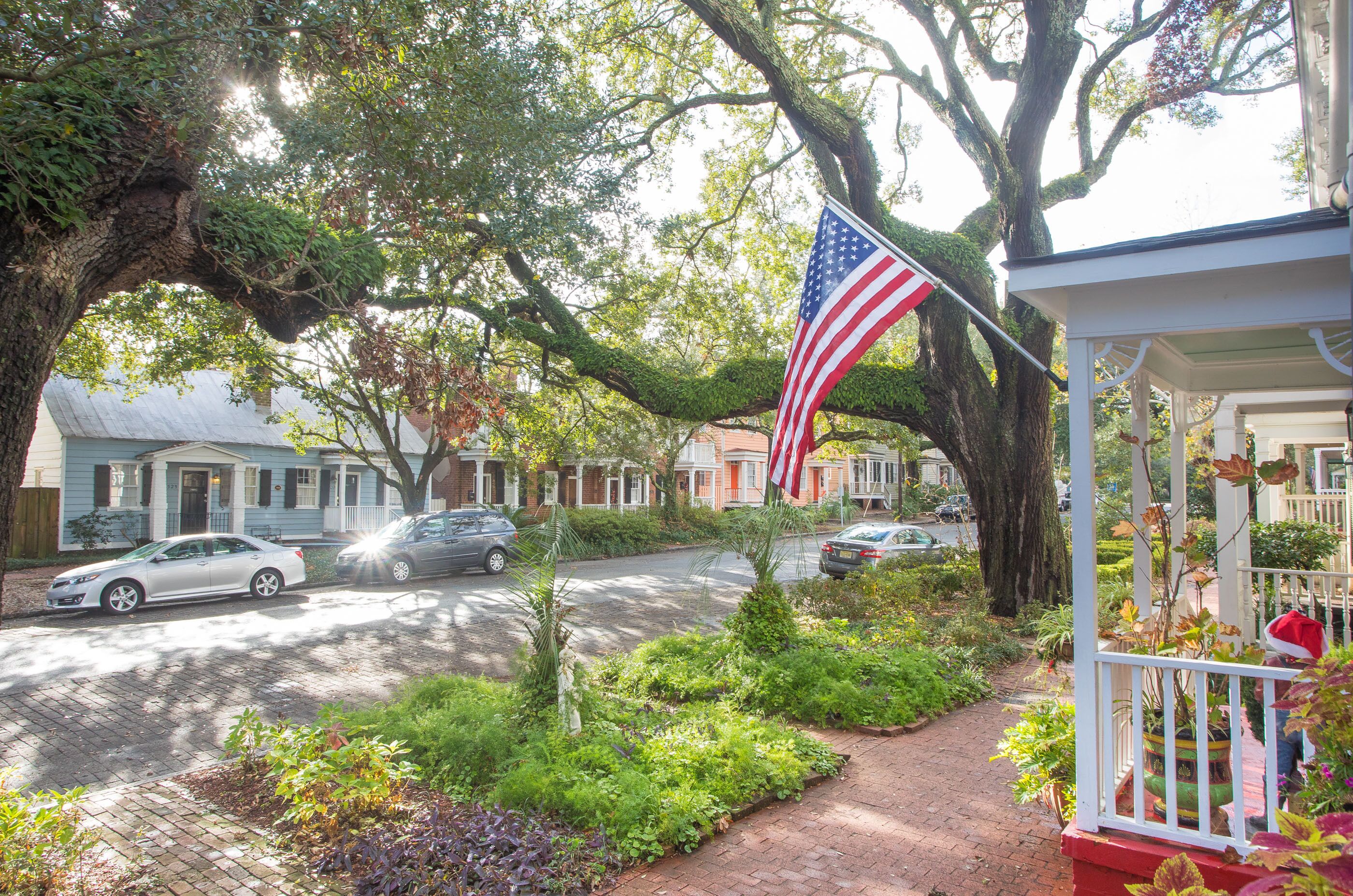 A residential street with houses, parked cars, and an American flag.