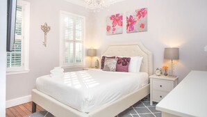 Une chambre avec un grand lit, des tables de chevet, un lustre et des œuvres d’art florales accrochées au mur.