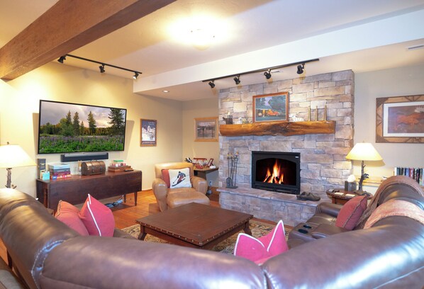 A living room with leather sofas, a stone fireplace, a flat-screen TV, and a bookshelf.