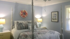 A four-poster bed with a floral-patterned bedspread, two bedside lamps, a wall-mounted wreath, and a framed picture on the wall. - Grace's Getaway: Newly refurbished.Two blocks to the beach! (Jekyll Island)