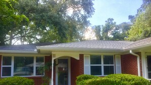 A single-story brick house with a covered front porch, a garage door, and a well-maintained lawn. - Grace's Getaway: Newly refurbished.Two blocks to the beach! (Jekyll Island)