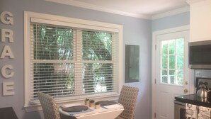 A kitchen with a dining area, featuring a window with blinds, a microwave, and a kettle on the stove. - Grace's Getaway: Newly refurbished.Two blocks to the beach! (Jekyll Island)