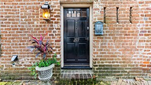 A black door with the number 217, a potted plant, and a lantern on a brick wall.