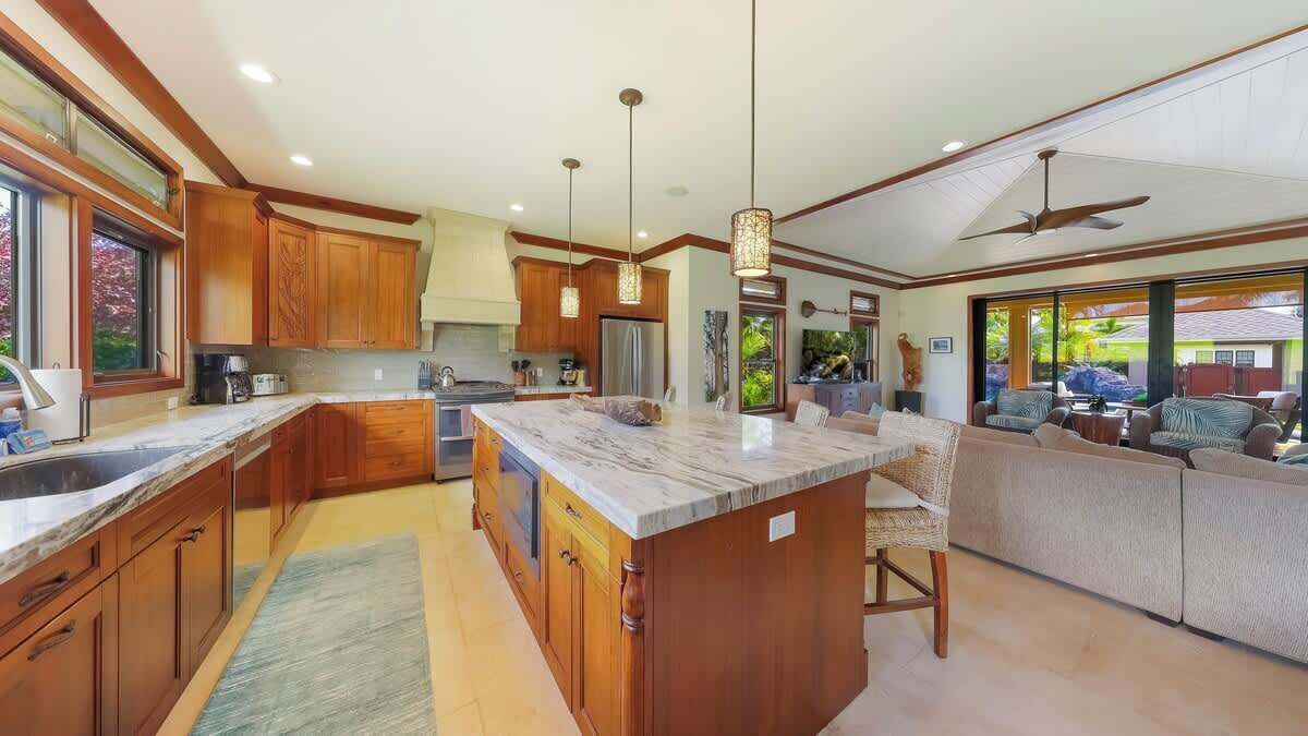 A spacious kitchen with wooden cabinets, a marble island, and pendant lighting.
