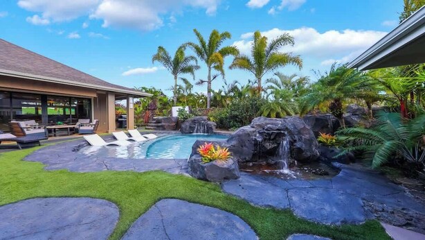 Ein Garten mit Swimmingpool, Liegestühlen, einem Wasserfall und tropischer Bepflanzung.
