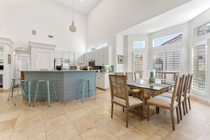 A spacious kitchen with white cabinetry, a central island with stools, and a dining area with wooden chairs. - 4BR Beach Villa with TWO GOLF CARTS!  Near Pool & Beach Tram. Screened Porch. (Miramar Beach)