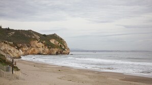 A beach with a rocky cliff and a staircase leading down to the shore.