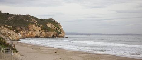 A beach with a rocky cliff and a staircase leading down to the shore.