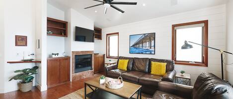 A modern living room with a leather sofa, a wooden coffee table, a fireplace, and a ceiling fan.