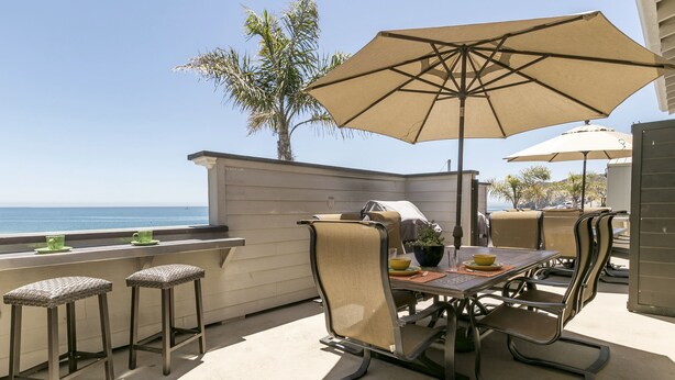 An outdoor patio with a table and chairs, a large umbrella, and a view of the ocean.