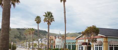 A street lined with palm trees and buildings with a mix of architectural styles, including a building with a sign that reads "OPEN".