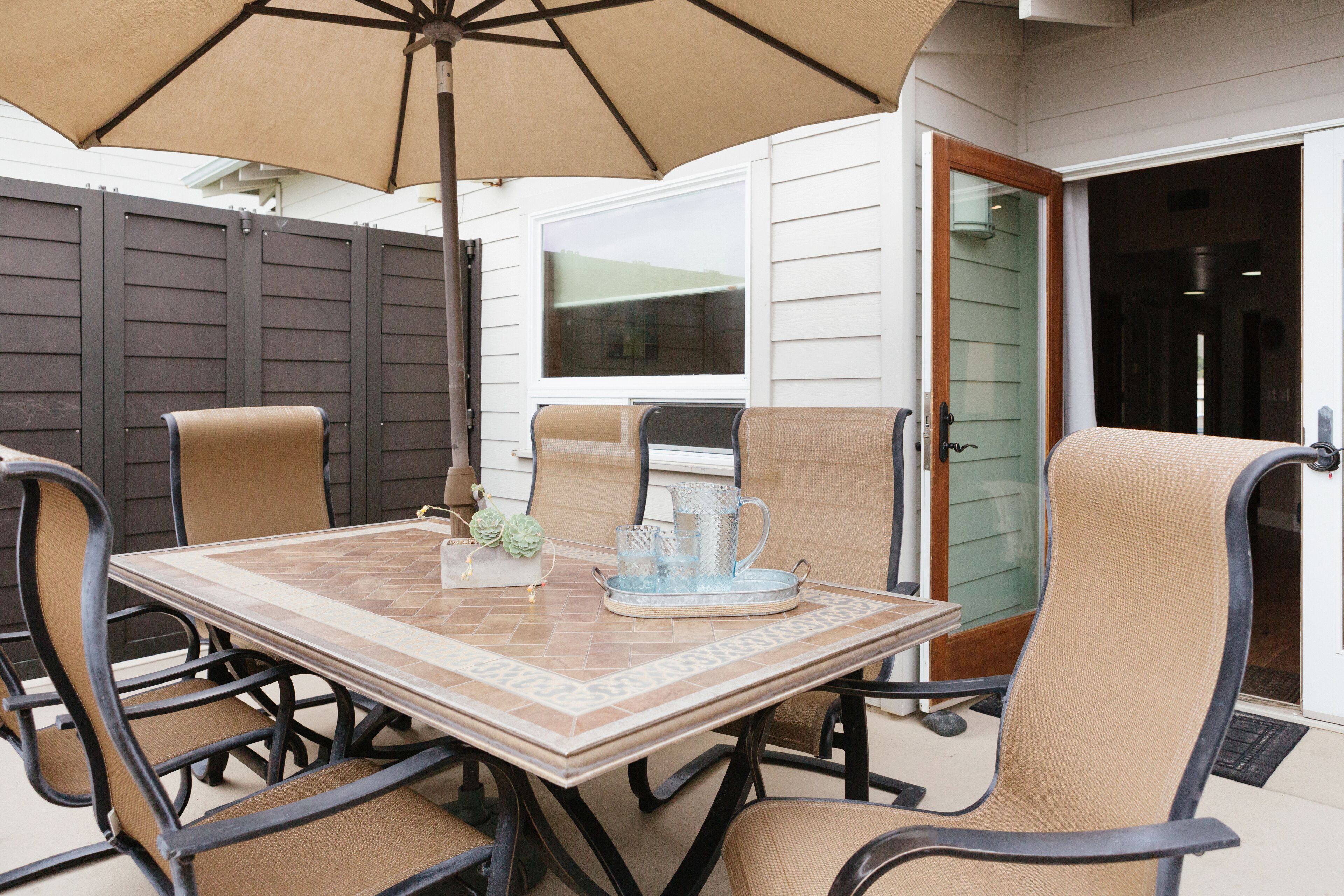 An outdoor patio with a table and chairs, a large umbrella, and a door leading to the interior.